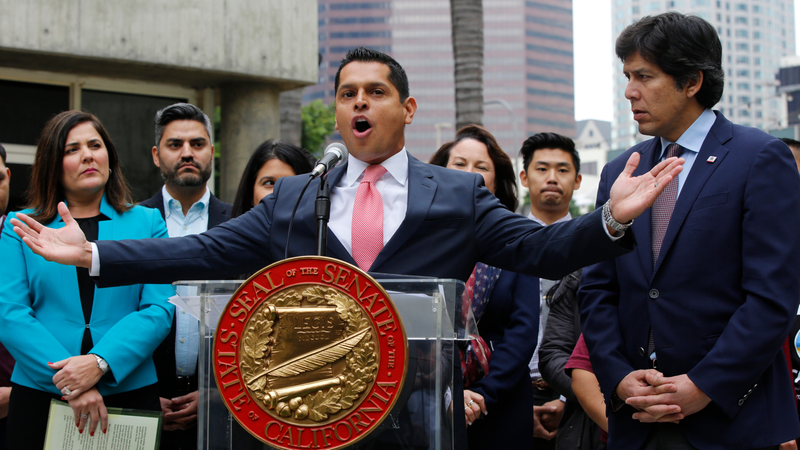 Assembly member Miguel Santiago (D-Los Angeles) at podium with State Sen. Kevin de Leon (D-Los Angeles), right, in Los Angeles Wednesday, Dec. 20, 2017.